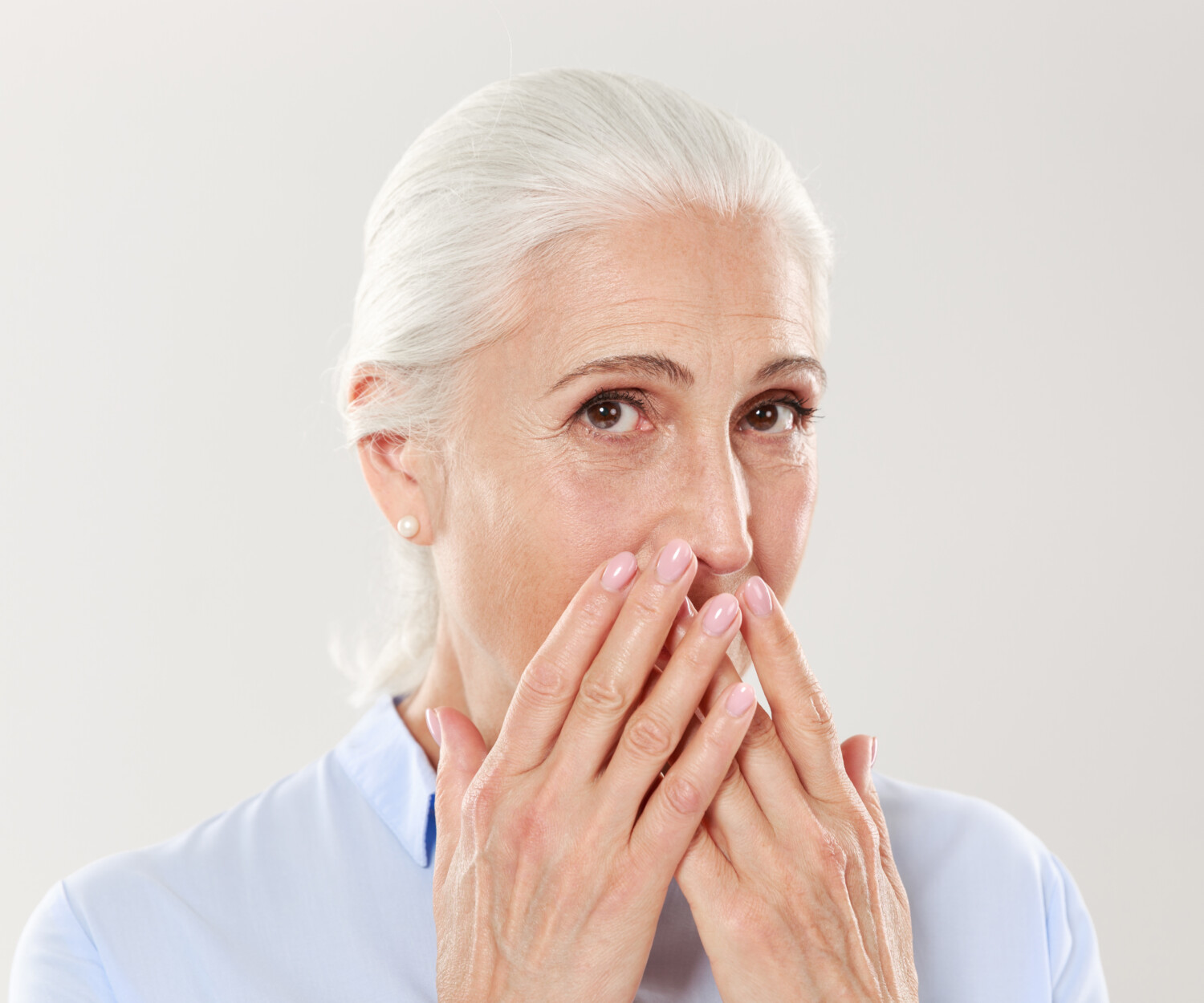 Close-up portrait of charming old lady, covering her mouth with hands, looking at camera, isolated over white background